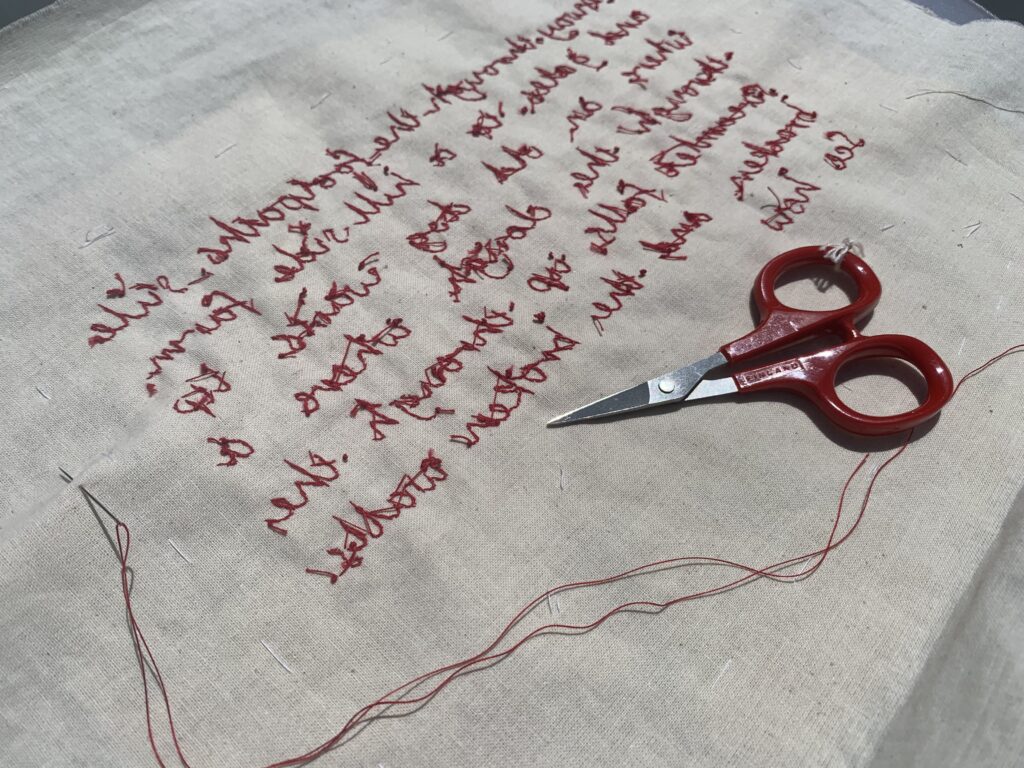 The reverse of the work showing red thread embroidery on cloth